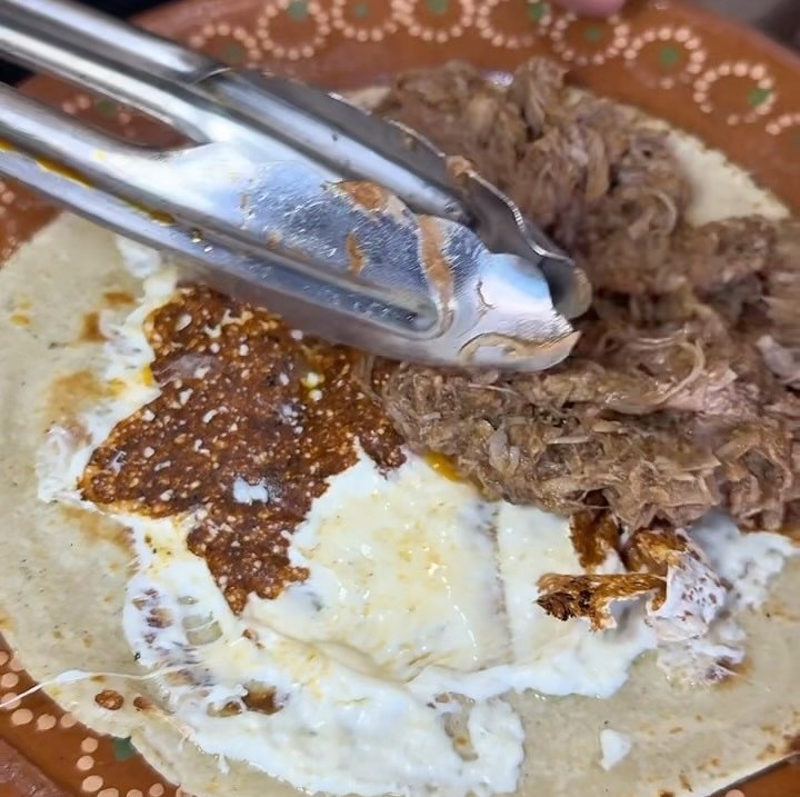 Barbacoa de res con queso sobre tortilla en plato de barro
